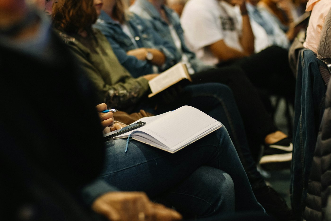 Gente sentada en una charla, con un cuaderno abierto